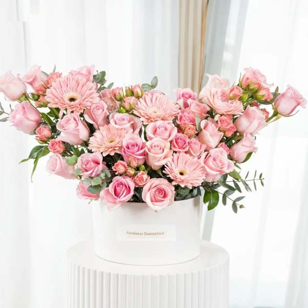 Pink roses and gerbera daisies arranged in a white hatbox