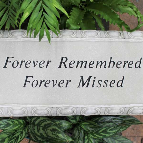 Memorial plaque with the words Forever Remembered Forever Missed surrounded by green plants