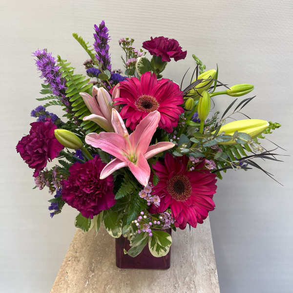Bouquet of pink lilies, magenta gerberas, and purple carnations in a square vase