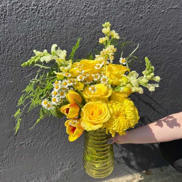 Yellow flower arrangement with roses, tulips, daisies, and mums in a yellow glass vase