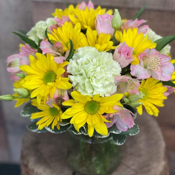 Bouquet of yellow daisies, pink alstroemeria, and white carnations in a glass vase
