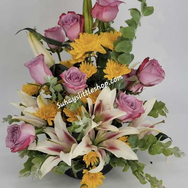 Arrangement of pink roses, yellow chrysanthemums, and white lilies in a low black container