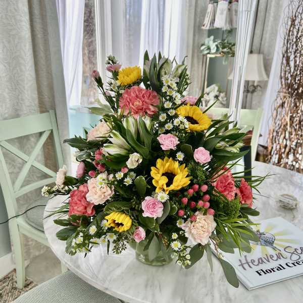 Mixed bouquet with sunflowers, pink carnations, and white daisies in a glass vase
