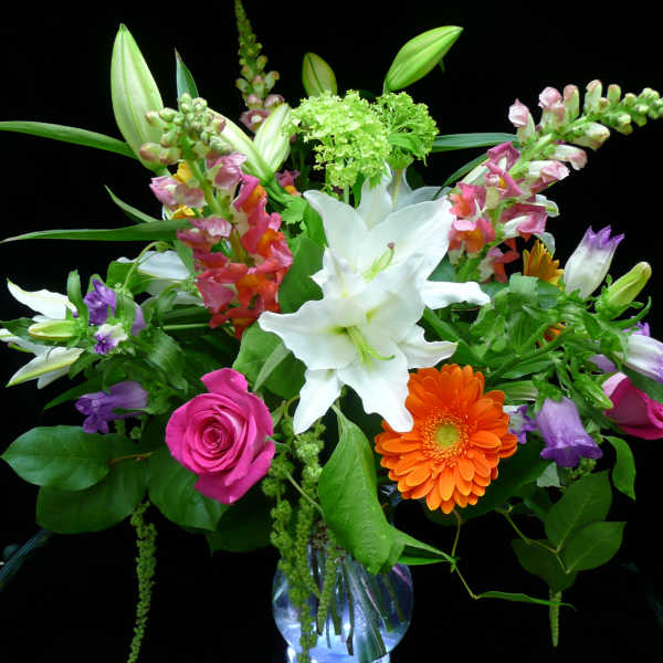 Mixed bouquet of white lilies, pink roses, and orange gerbera in a clear glass vase.