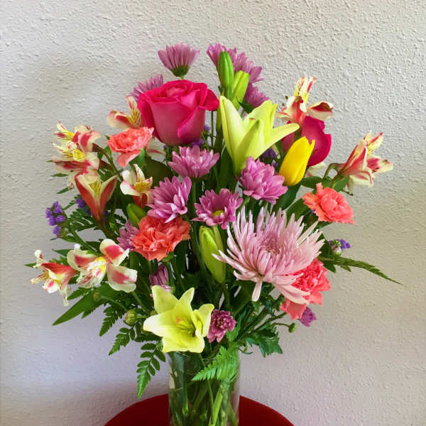 Mixed bouquet in a clear glass vase with pink roses, lilies, and daisies
