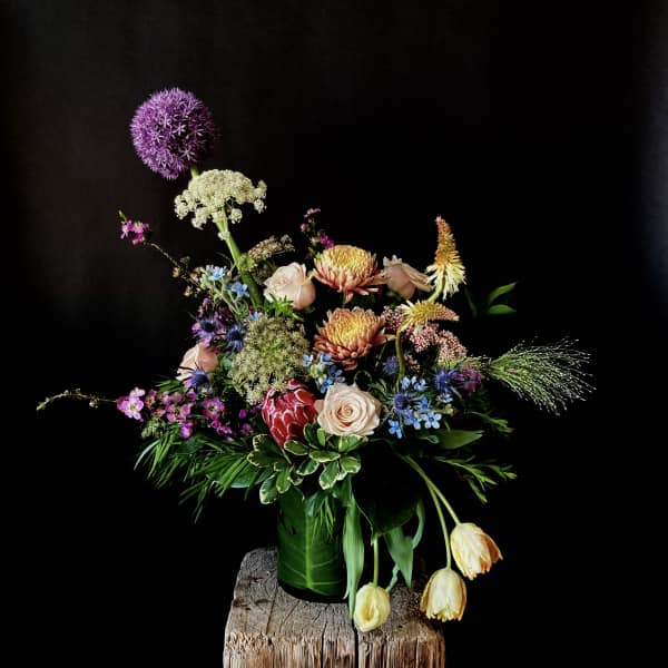 Mixed floral arrangement with roses, tulips, and purple allium in a green vase