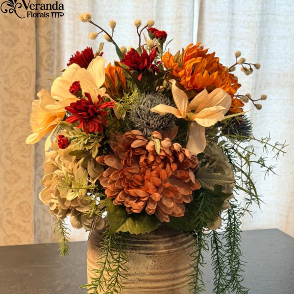 Autumn-toned mixed flower arrangement in a rustic ceramic vase with trailing greenery.