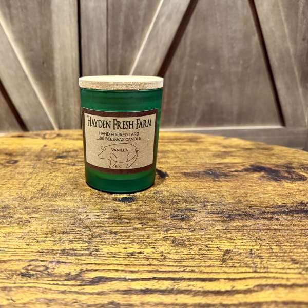 Green glass candle jar with a beige label on a wooden surface