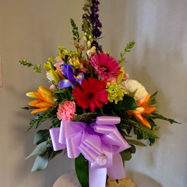 Colorful mixed flower arrangement with a lavender bow in a vase