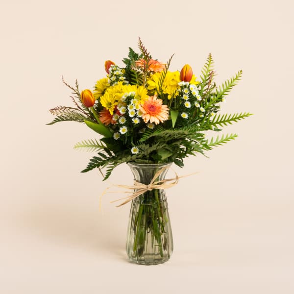 Mixed bouquet of yellow and peach flowers in a glass vase