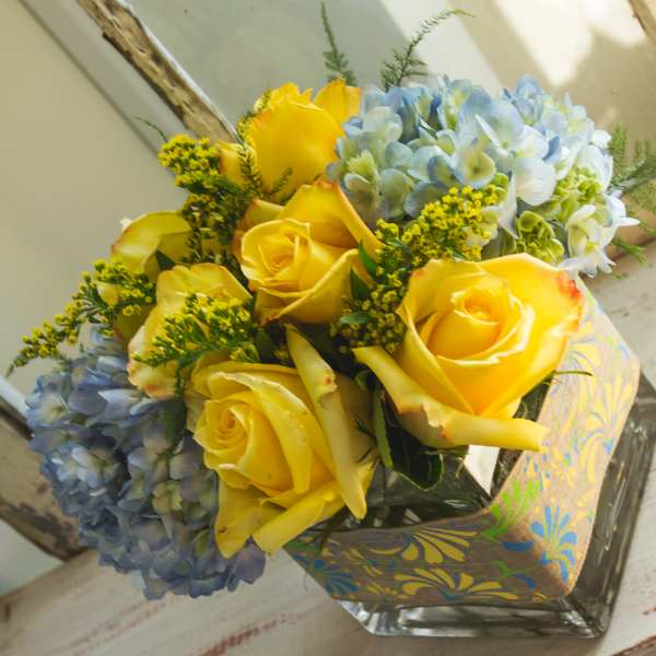 Yellow roses and blue hydrangeas in a square glass vase