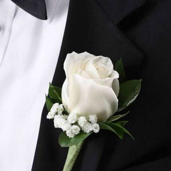 White rose boutonniere with small white filler flowers pinned to a black suit lapel