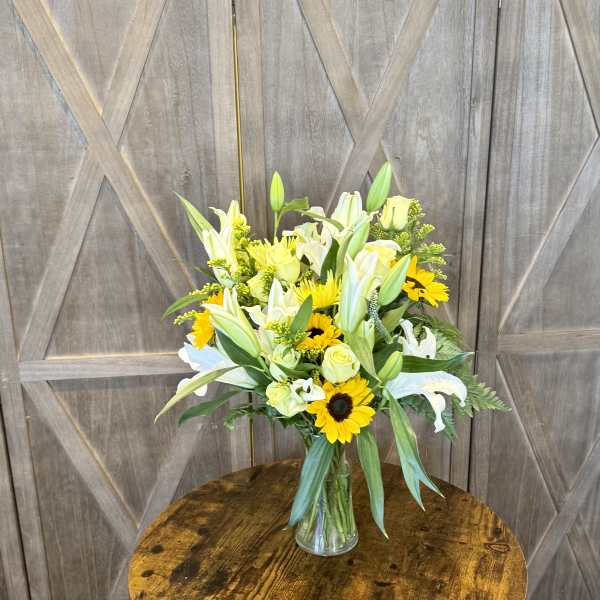 Bouquet of white lilies, yellow roses, and sunflowers in a clear glass vase