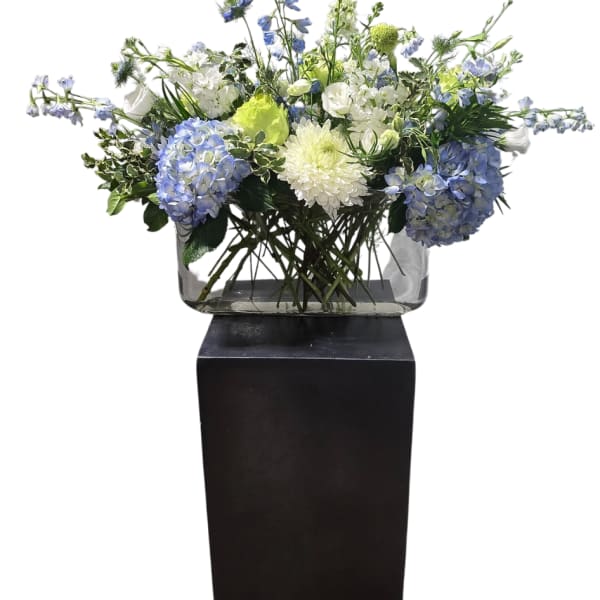 Blue and white floral arrangement in a clear rectangular vase on a black pedestal