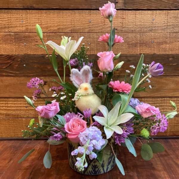 Pink and white floral arrangement with a small bunny decoration in a patterned container