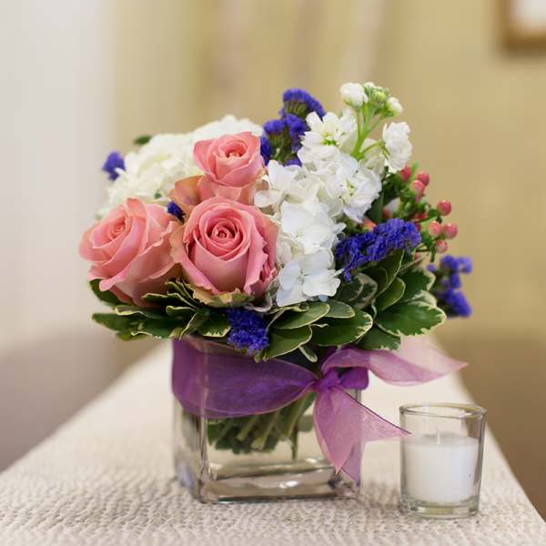Pink roses and white flowers in a glass vase with a purple ribbon