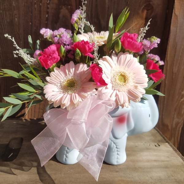 Pink and white flowers arranged in a small elephant-shaped vase with a ribbon
