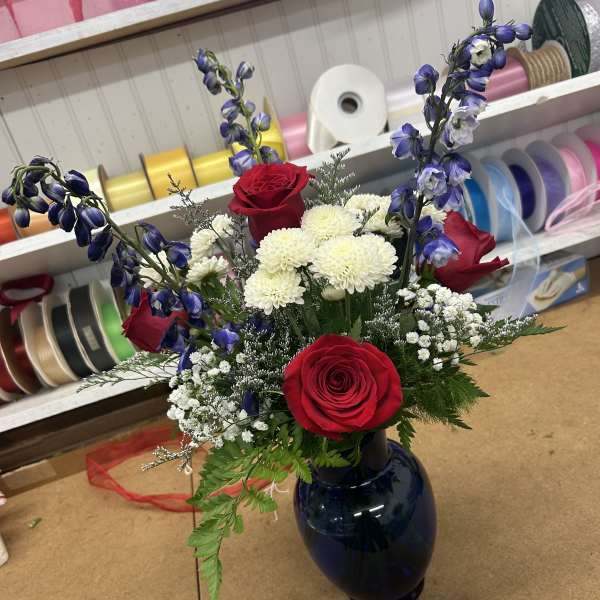 Red roses and white mums in a dark blue vase with blue delphinium