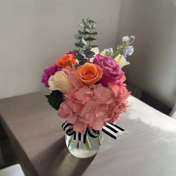 Pink and orange flower arrangement in a glass vase with a striped ribbon