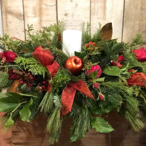 Holiday centerpiece with a white candle, red roses, and evergreen foliage