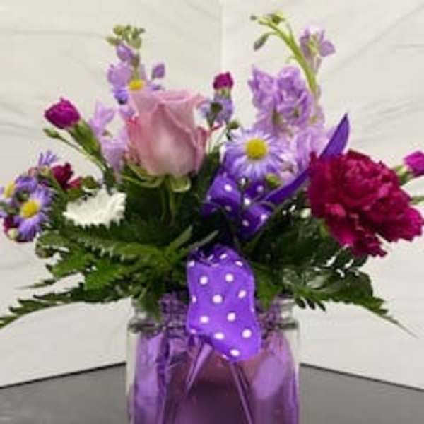 Mixed purple and pink flowers in a glass vase with a purple ribbon