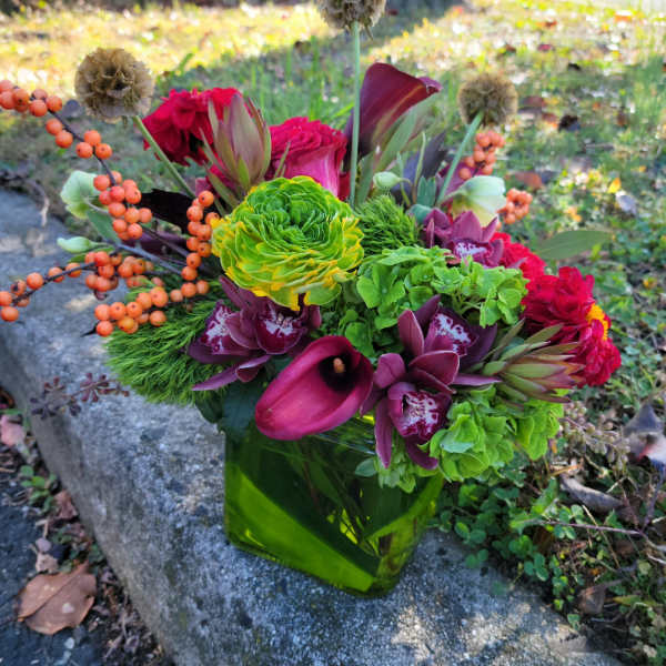 Colorful mixed bouquet in a green glass vase with calla lilies and orchids