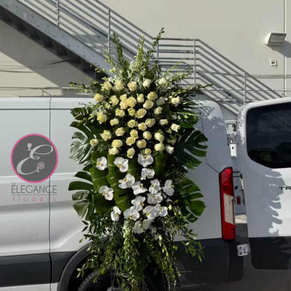 Tall white rose and orchid standing spray with large tropical leaves