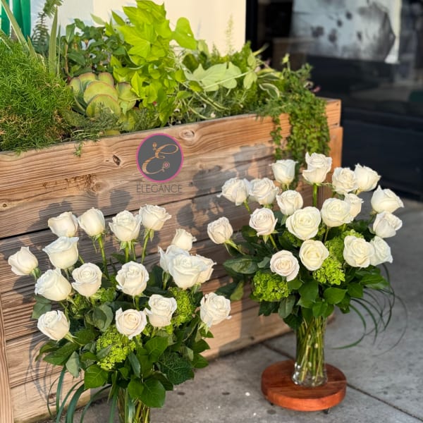 Two white rose arrangements in glass vases with green accents