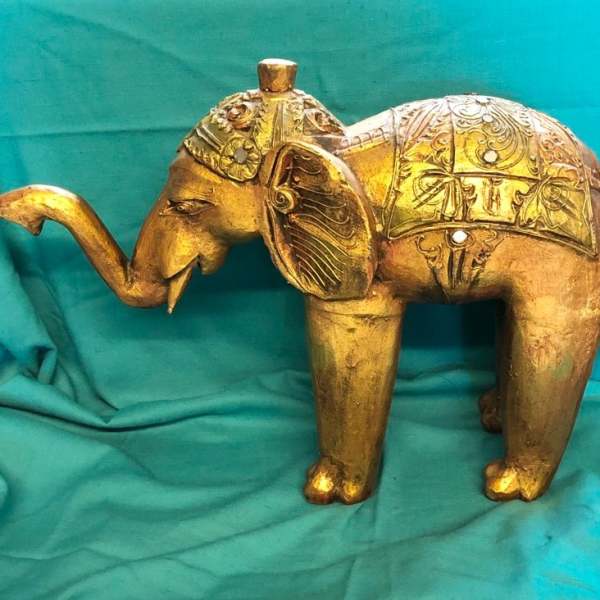 Gold elephant figurine with ornate carved details on a teal cloth background
