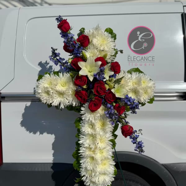Cross-shaped floral tribute with red roses, white chrysanthemums, and blue flowers