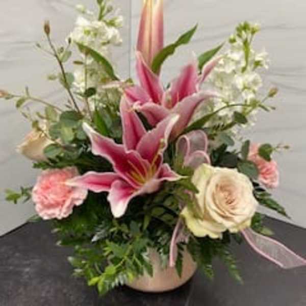 Pink lilies and roses arranged in a low vase with white filler flowers.