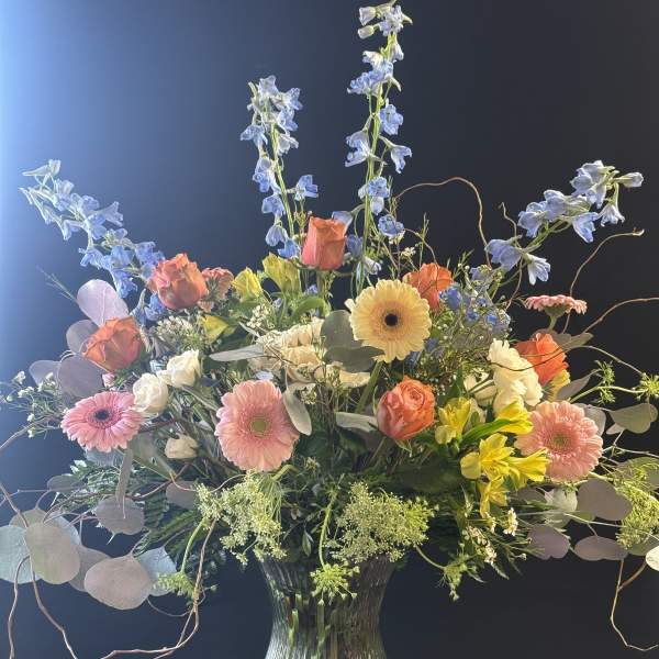 Mixed bouquet in a glass vase with blue delphinium and pink gerbera daisies