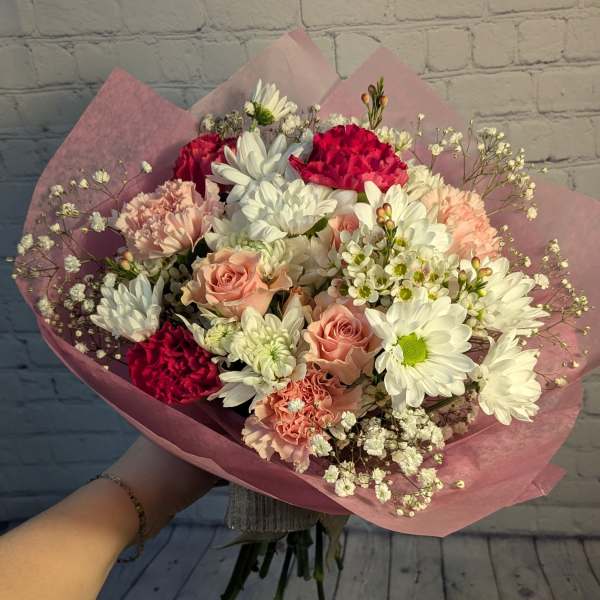 Handheld bouquet of white daisies, pink roses, and carnations wrapped in pink paper