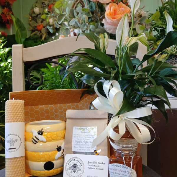 Gift set with a floral arrangement, candle, honey jar, and packaged herbal items