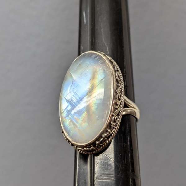 Oval iridescent gemstone ring on a dark display stand
