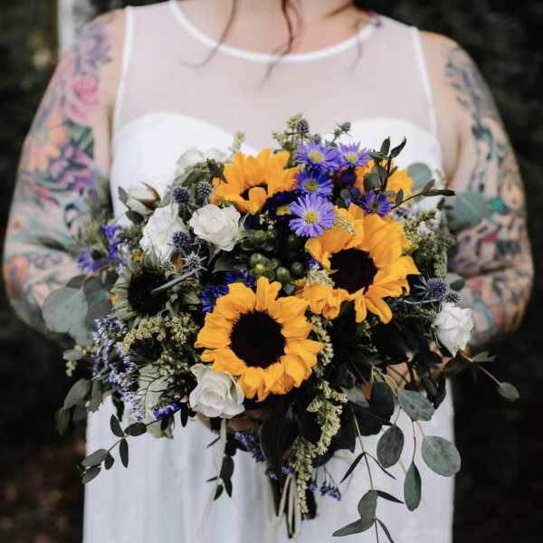 Bride holding a bouquet of sunflowers, white roses, and purple flowers