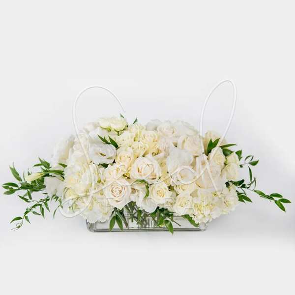 Low rectangular centerpiece of ivory roses and white blooms in a clear glass vase