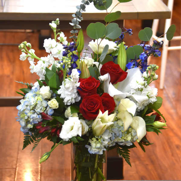 Tall red, white, and blue mixed flower arrangement in a clear rectangular glass vase