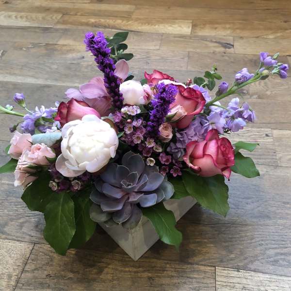 Mixed pink and purple flower arrangement in a square box