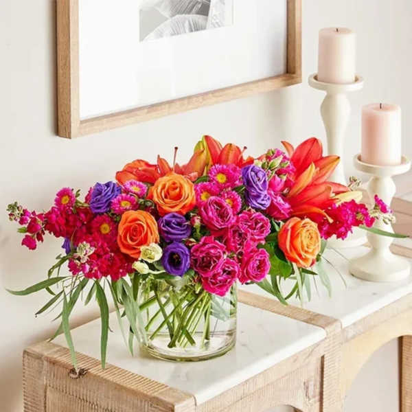 Bright mixed bouquet in a clear glass vase beside two candles