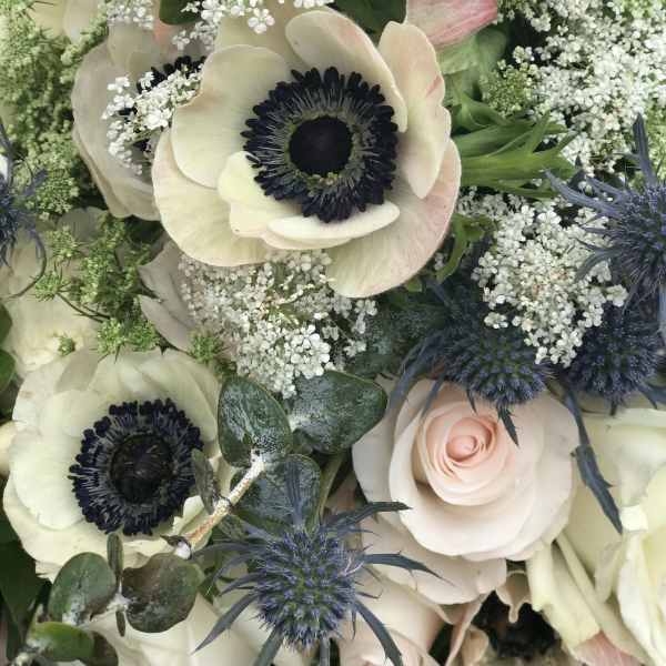 Bouquet of white anemones, pale roses, and blue thistles