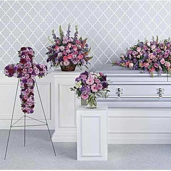 Floral casket spray and standing arrangements in pink and purple around a white casket
