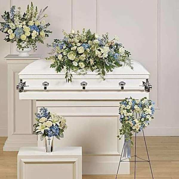 White casket with blue and cream floral sprays in a funeral setting