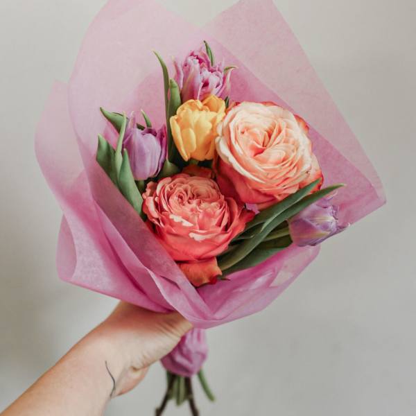 Handheld bouquet of pink and peach tulips wrapped in pink paper