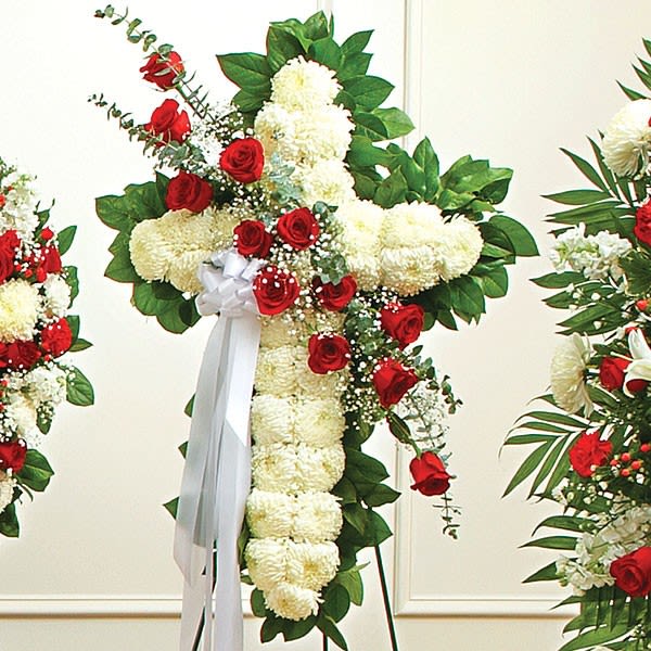 Standing floral cross with white blooms, red roses, and a white ribbon