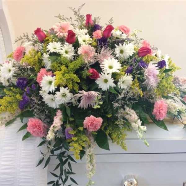 Large pink, white, and purple floral spray on a white casket