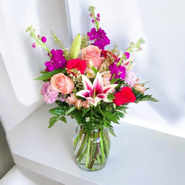 Mixed bouquet of pink roses, lilies, and purple blooms in a glass vase