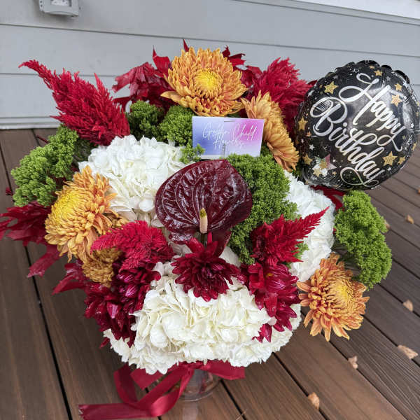 Mixed red, white, and orange floral arrangement with a birthday balloon