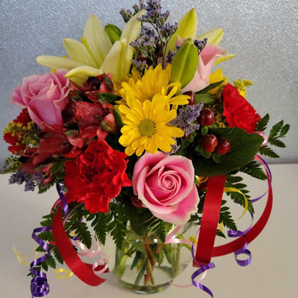 Mixed bouquet of pink roses, lilies, and yellow daisies in a glass vase