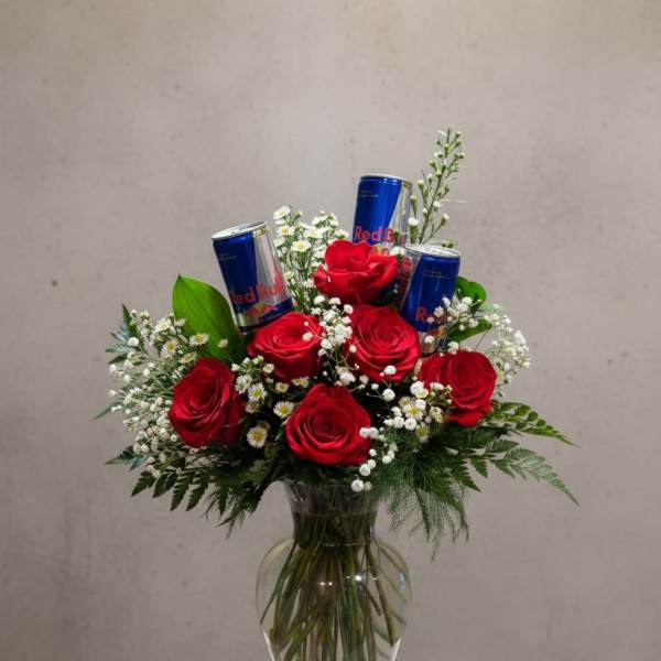 Red roses in a glass vase with Red Bull cans and small white filler flowers